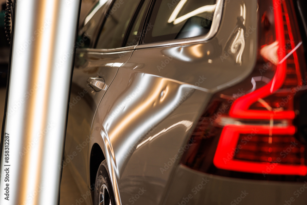A silver car with a red brake light is parked in a garage with hail damage problems