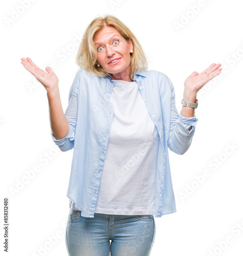 Middle age blonde woman over isolated background clueless and confused expression with arms and hands raised. Doubt concept.