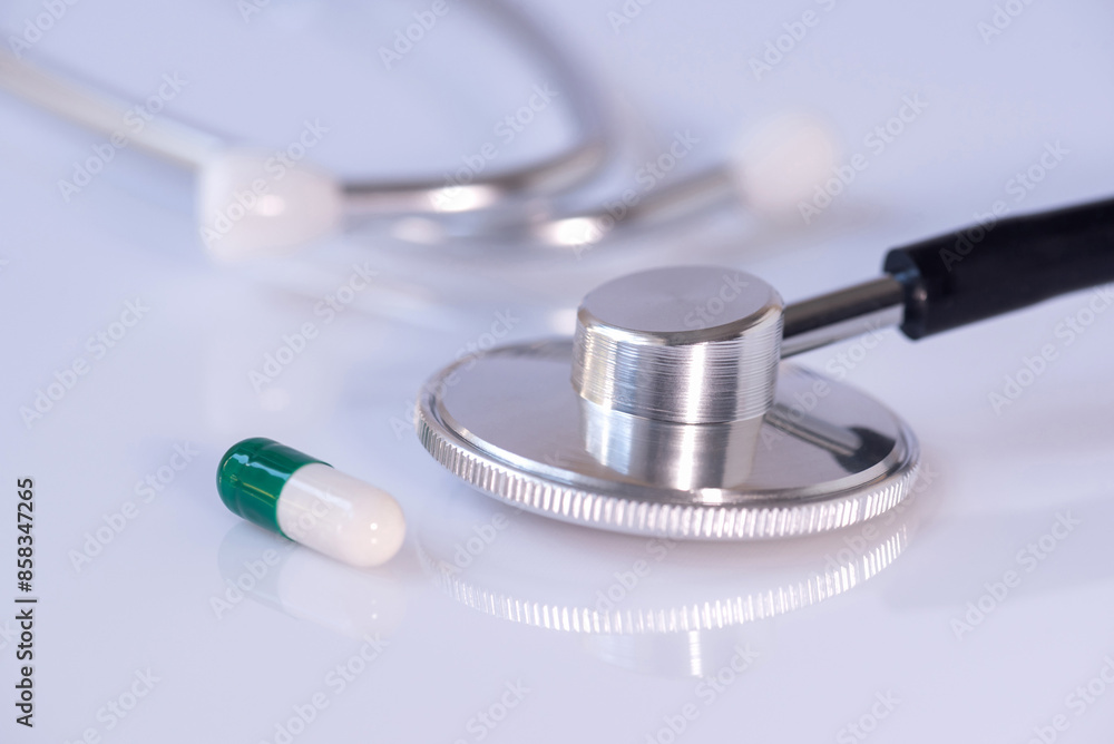 A stethoscope and a green medical pill in a capsule on a white plastic background. Phonendoscope. Pharmaceutical industry. Healthcare. A stethoscope and a green medical pill in a capsule on a white plastic background. Phonendoscope. Pharmaceutical industry. Healthcare.