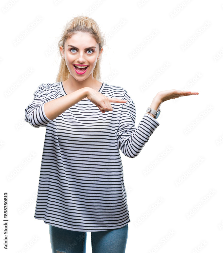 Young beautiful blonde woman wearing stripes sweater over isolated background amazed and smiling to the camera while presenting with hand and pointing with finger. Young beautiful blonde woman wearing stripes sweater over isolated background amazed and smiling to the camera while presenting with hand and pointing with finger.