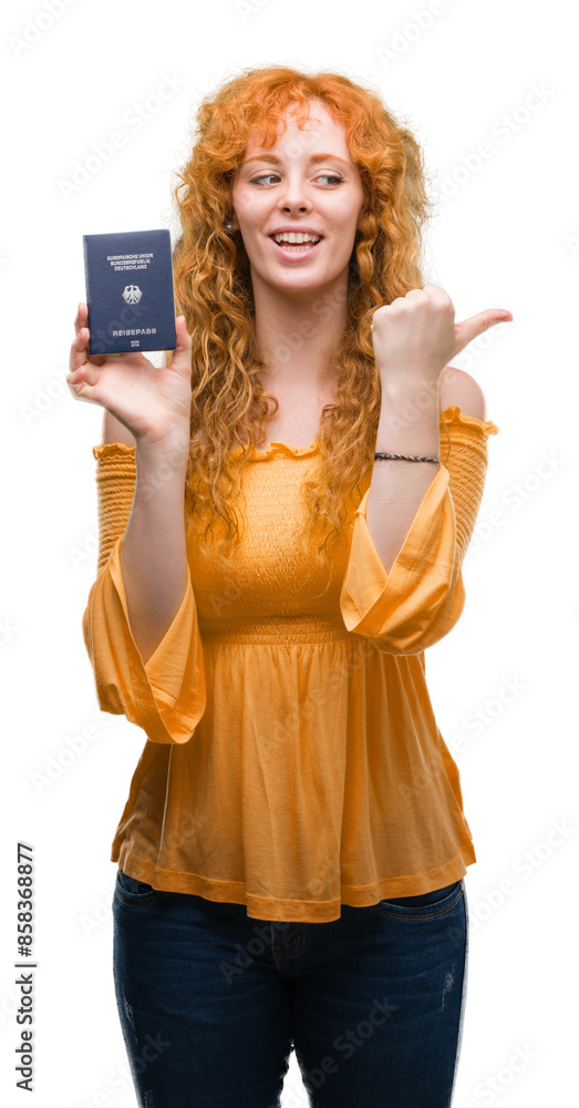 Young redhead woman holding passport of Germany pointing and showing with thumb up to the side with happy face smiling Young redhead woman holding passport of Germany pointing and showing with thumb up to the side with happy face smiling