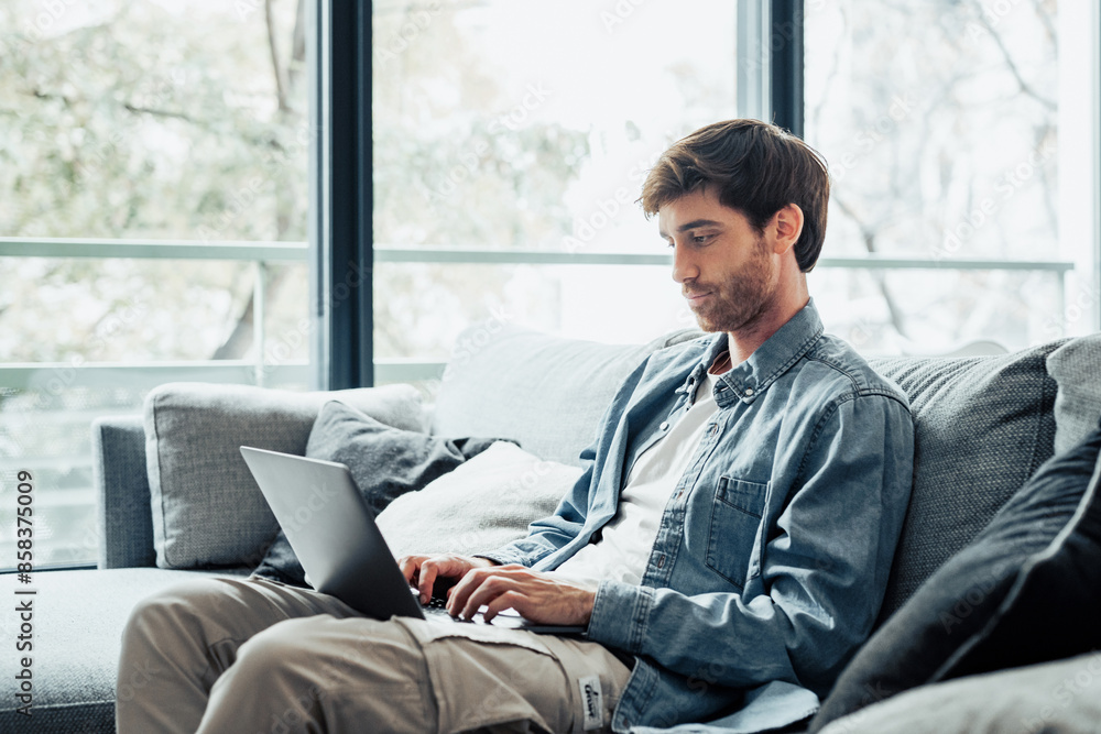 Handsome serious man sits on sofa with computer on laps, spend time at home web surfing information, use modern tech, make order on internet. Freelancing, telework, new software learning, tech concept Handsome serious man sits on sofa with computer on laps, spend time at home web surfing information, use modern tech, make order on internet. Freelancing, telework, new software learning, tech concept