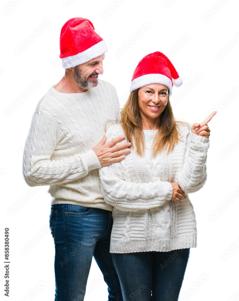 Middle age hispanic couple wearing christmas hat over isolated background with a big smile on face, pointing with hand and finger to the side looking at the camera. Middle age hispanic couple wearing christmas hat over isolated background with a big smile on face, pointing with hand and finger to the side looking at the camera.