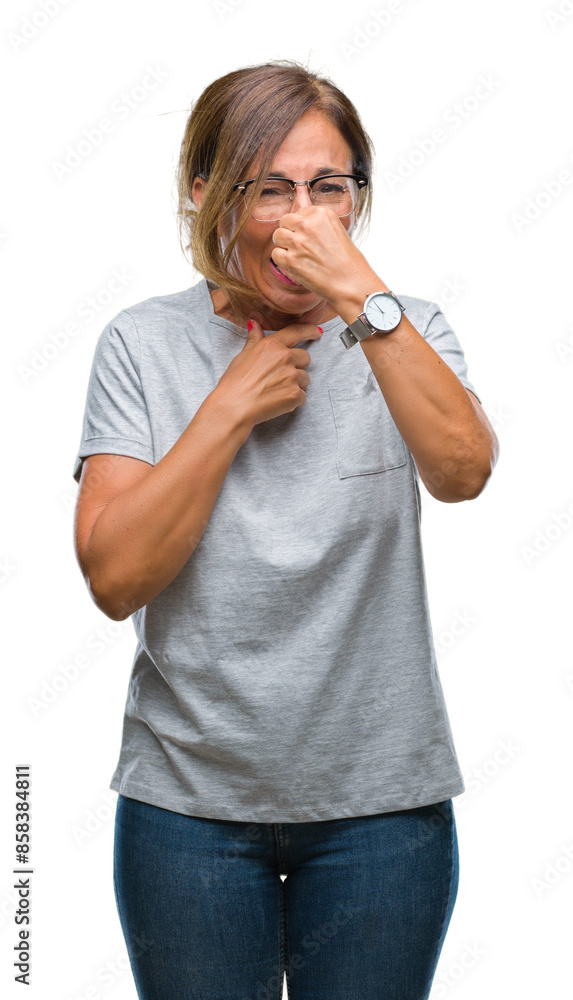 Middle age senior hispanic woman wearing glasses over isolated background smelling something stinky and disgusting, intolerable smell, holding breath with fingers on nose. Bad smells concept. Middle age senior hispanic woman wearing glasses over isolated background smelling something stinky and disgusting, intolerable smell, holding breath with fingers on nose. Bad smells concept.