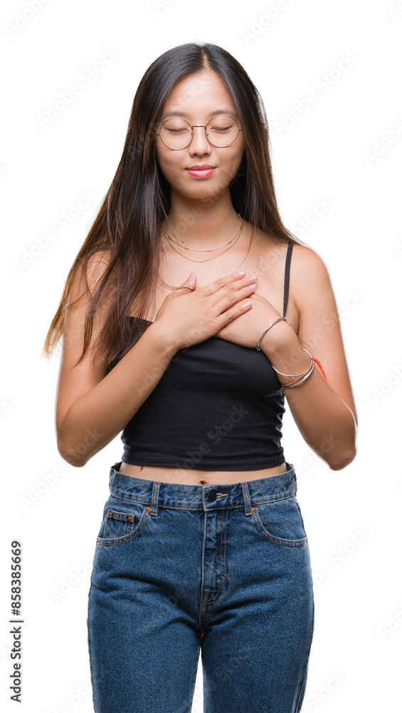 Young asian woman wearing glasses over isolated background smiling with hands on chest with closed eyes and grateful gesture on face. Health concept. Young asian woman wearing glasses over isolated background smiling with hands on chest with closed eyes and grateful gesture on face. Health concept.