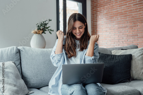 Tableau sur toile Excited emotional screams with joy woman sit on sofa hold on lap notebook makes Yes hand gesture feels happy getting job of dream, e-mail sales discount special offer, on-line lottery victory concept