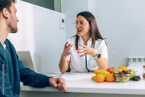 Obraz na plátně Beautiful young nutritionist woman explaining to her patient the diet he should follow to lose weight in the consultation