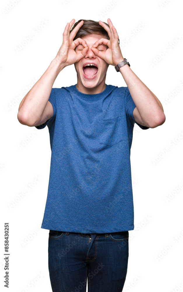 Naklejka premium Young handsome man wearing blue t-shirt over isolated background doing ok gesture like binoculars sticking tongue out, eyes looking through fingers. Crazy expression.