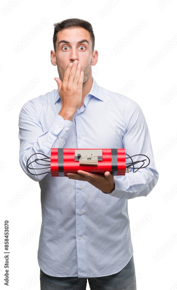 Handsome young business man holding an alarm clock bomb cover mouth with hand shocked with shame for mistake, expression of fear, scared in silence, secret concept