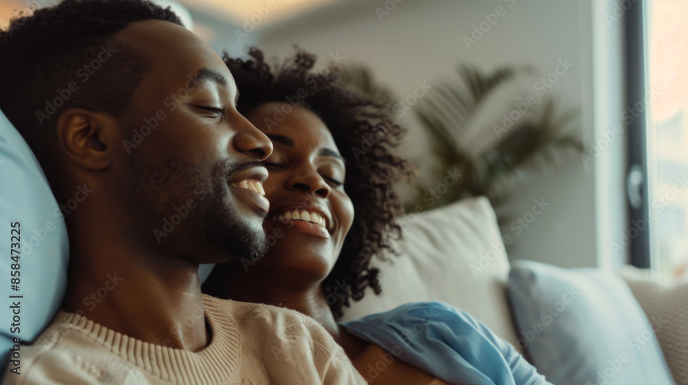 Obraz premium Portrait of a beautiful African American couple spending time together on the sofa in the living room. Young man and woman enjoying each other indoors. Love concept.
