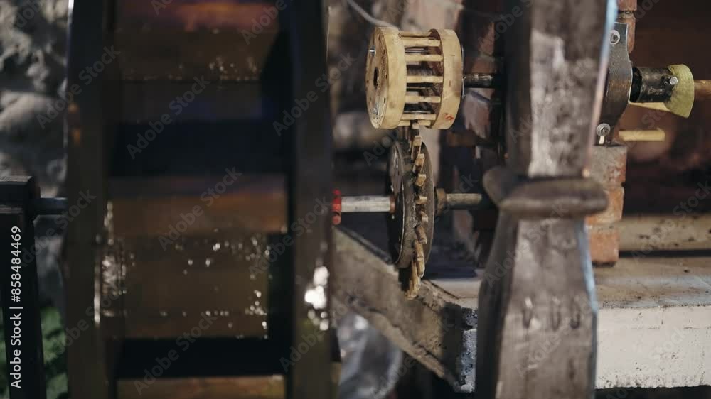 Detailed view of a rotating mechanism in an ancient water mill, featuring gears and flowing water in a rustic setting. Detailed view of a rotating mechanism in an ancient water mill, featuring gears and flowing water in a rustic setting.