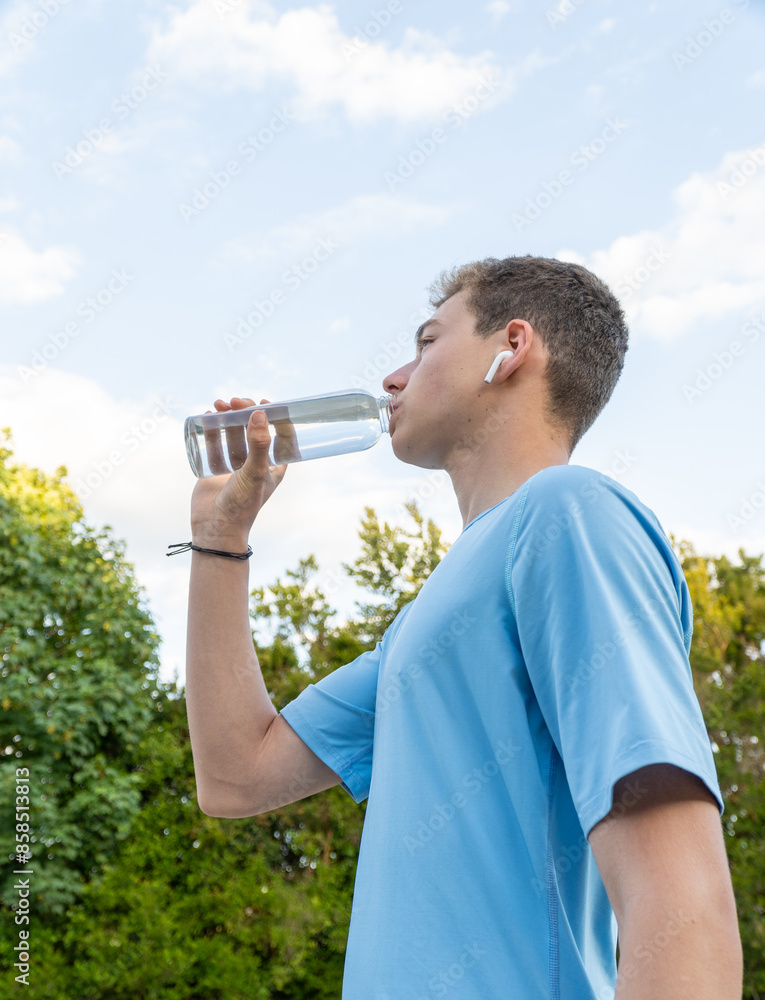 Teenager drinking water from a glass bottle while training outdoors. Teenager drinking water from a glass bottle while training outdoors.