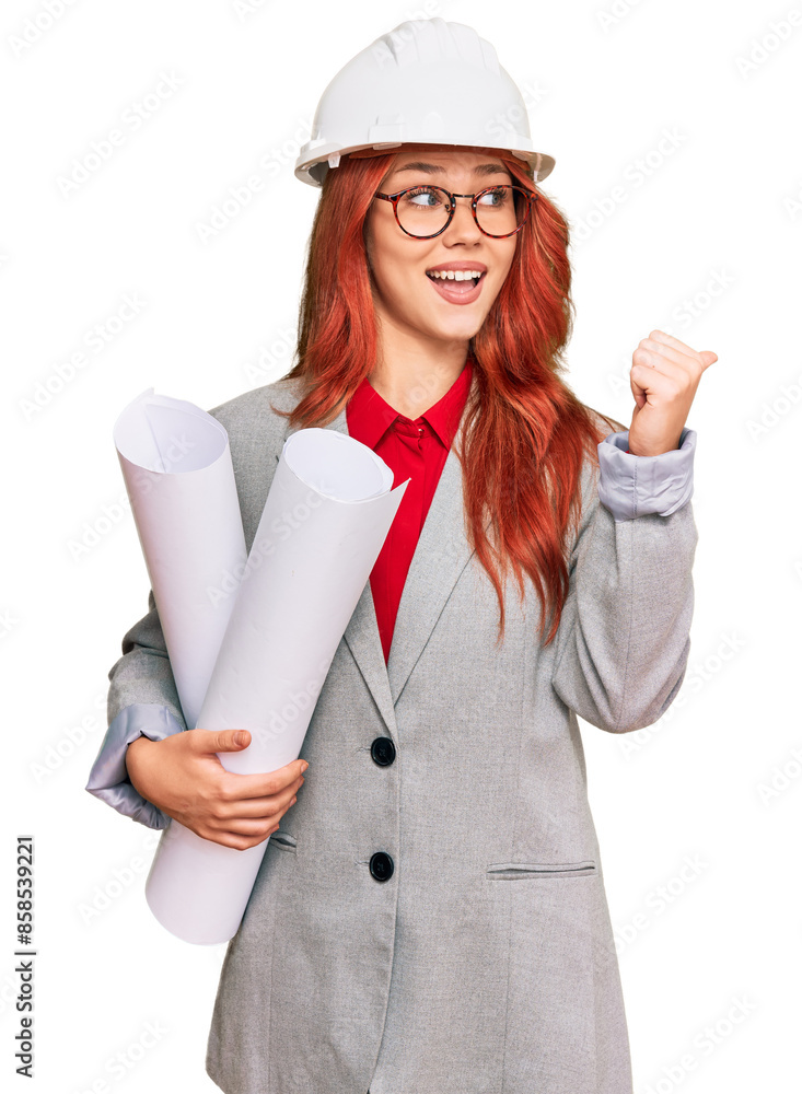 Young redhead architect woman wearing safety helmet holding blueprints pointing thumb up to the side smiling happy with open mouth Young redhead architect woman wearing safety helmet holding blueprints pointing thumb up to the side smiling happy with open mouth