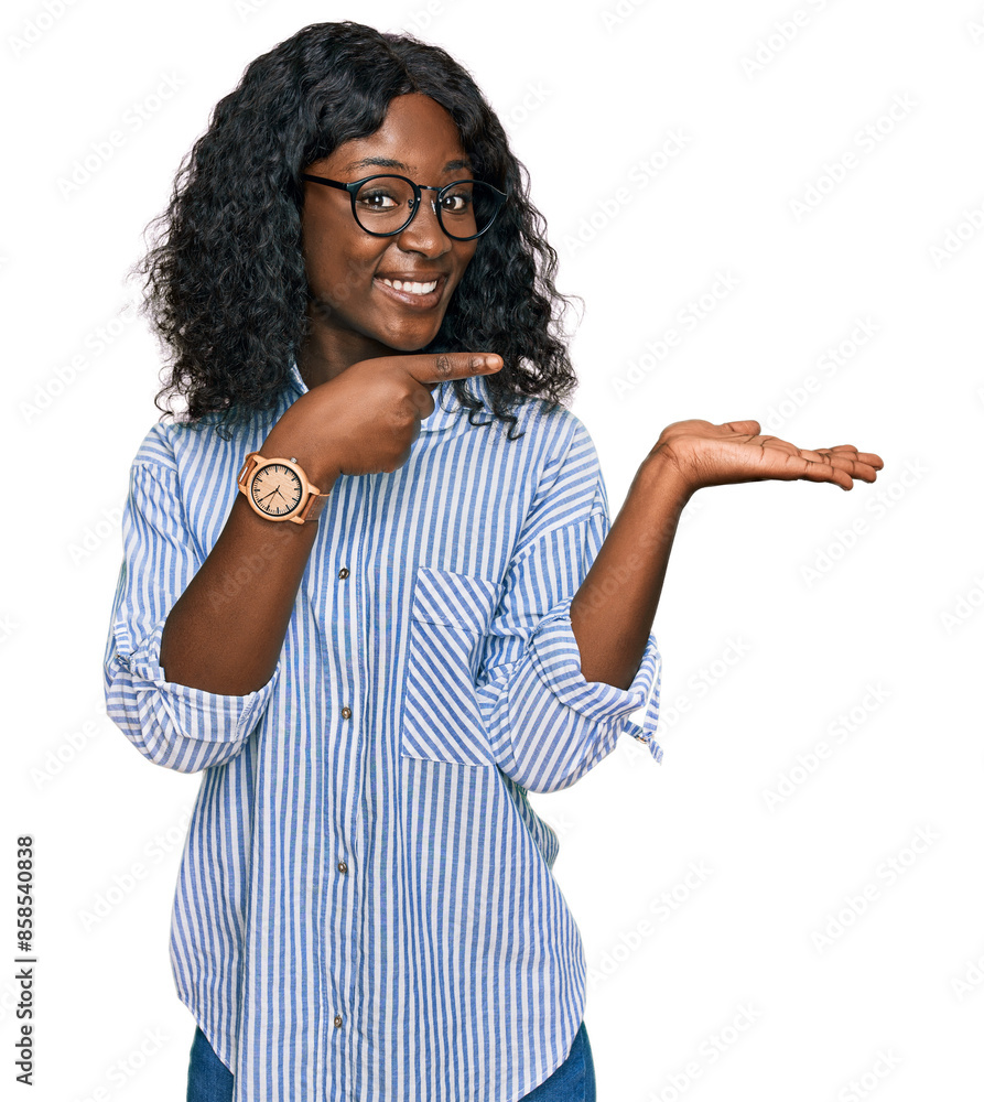 Beautiful african young woman wearing casual clothes and glasses amazed and smiling to the camera while presenting with hand and pointing with finger. Beautiful african young woman wearing casual clothes and glasses amazed and smiling to the camera while presenting with hand and pointing with finger.