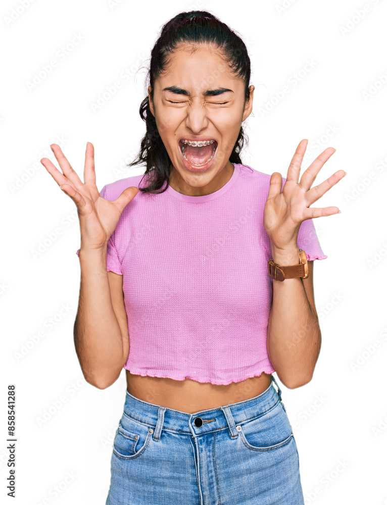 Hispanic teenager girl with dental braces wearing casual clothes celebrating mad and crazy for success with arms raised and closed eyes screaming excited. winner concept Hispanic teenager girl with dental braces wearing casual clothes celebrating mad and crazy for success with arms raised and closed eyes screaming excited. winner concept