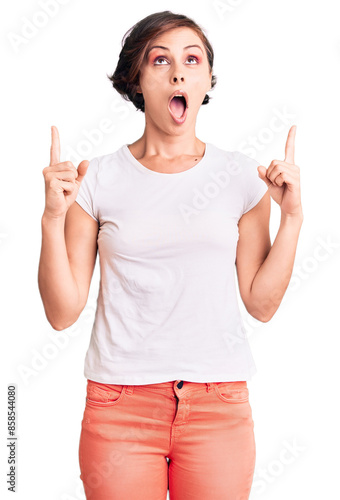 Beautiful young woman with short hair wearing casual clothes amazed and surprised looking up and pointing with fingers and raised arms.