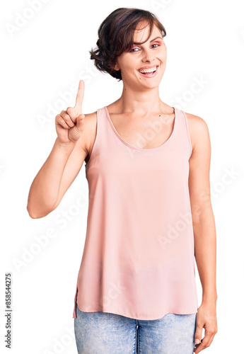 Beautiful young woman with short hair wearing casual style with sleeveless shirt showing and pointing up with finger number one while smiling confident and happy.