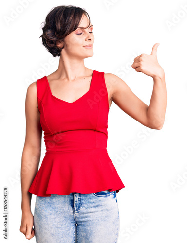 Beautiful young woman with short hair wearing casual style with sleeveless shirt looking proud, smiling doing thumbs up gesture to the side