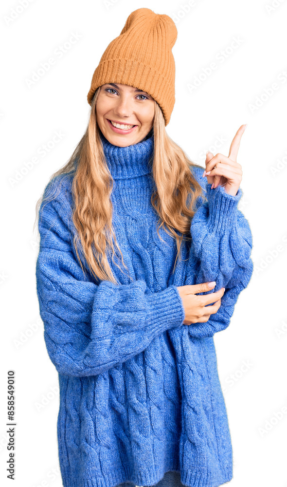 Beautiful caucasian woman with blonde hair wearing wool sweater and winter hat smiling happy pointing with hand and finger to the side Beautiful caucasian woman with blonde hair wearing wool sweater and winter hat smiling happy pointing with hand and finger to the side