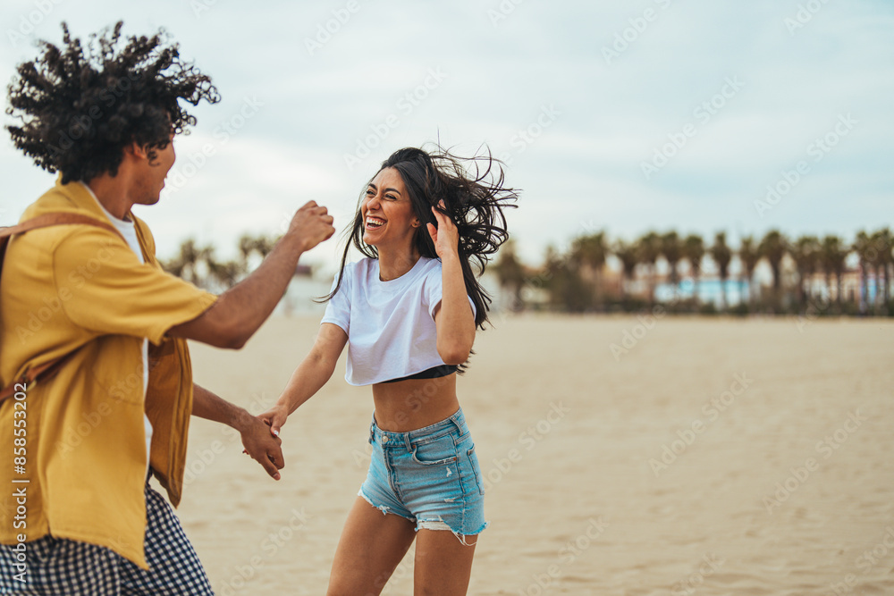 A young adult Hispanic couple laughs together, enjoying a playful moment on a sandy beach, dressed in casual summer attire, under an overcast sky. A young adult Hispanic couple laughs together, enjoying a playful moment on a sandy beach, dressed in casual summer attire, under an overcast sky.