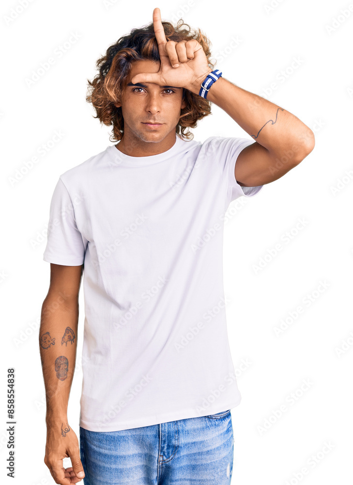 Young hispanic man wearing casual white tshirt making fun of people with fingers on forehead doing loser gesture mocking and insulting. Young hispanic man wearing casual white tshirt making fun of people with fingers on forehead doing loser gesture mocking and insulting.