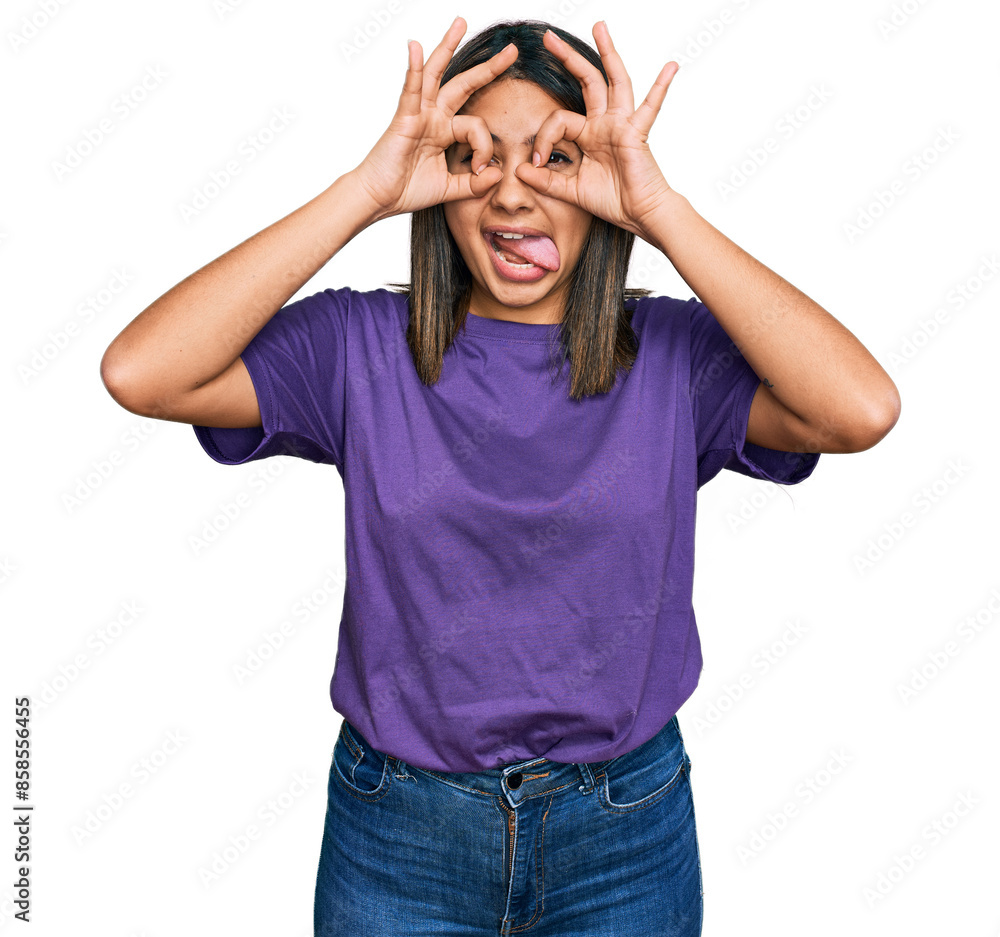 Young hispanic girl wearing casual purple t shirt doing ok gesture like binoculars sticking tongue out, eyes looking through fingers. crazy expression. Young hispanic girl wearing casual purple t shirt doing ok gesture like binoculars sticking tongue out, eyes looking through fingers. crazy expression.