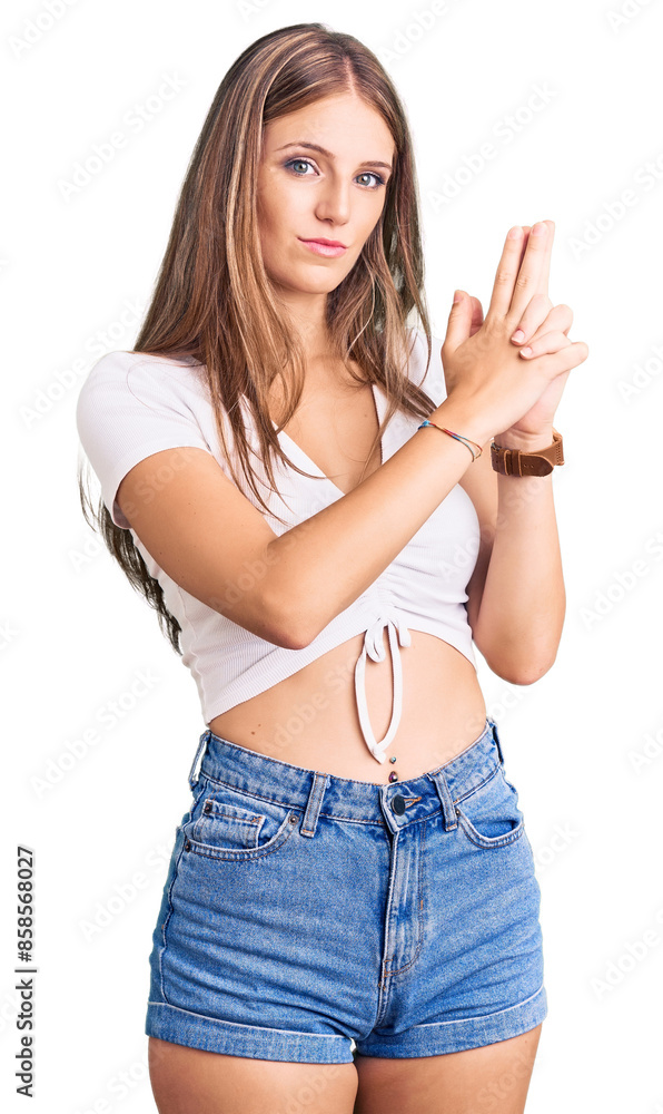Young beautiful blonde woman wearing casual white tshirt holding symbolic gun with hand gesture, playing killing shooting weapons, angry face Young beautiful blonde woman wearing casual white tshirt holding symbolic gun with hand gesture, playing killing shooting weapons, angry face