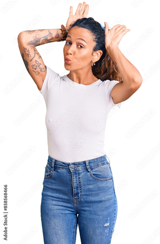 Young hispanic woman with tattoo wearing casual white tshirt doing bunny ears gesture with hands palms looking cynical and skeptical. easter rabbit concept. Young hispanic woman with tattoo wearing casual white tshirt doing bunny ears gesture with hands palms looking cynical and skeptical. easter rabbit concept.