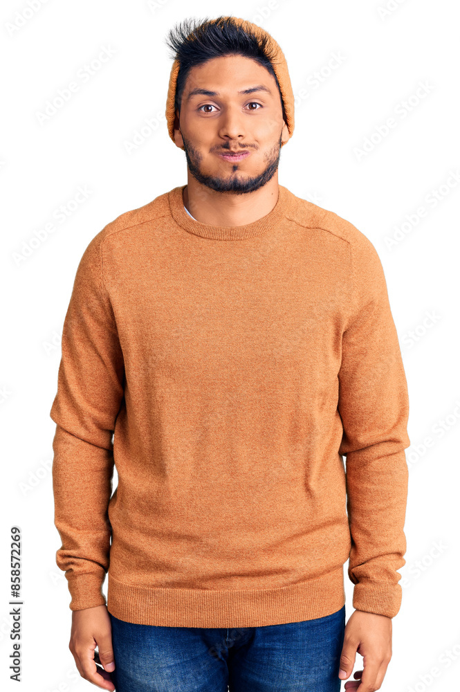 Handsome latin american young man wearing winter sweater and wool hat puffing cheeks with funny face. mouth inflated with air, crazy expression. Handsome latin american young man wearing winter sweater and wool hat puffing cheeks with funny face. mouth inflated with air, crazy expression.
