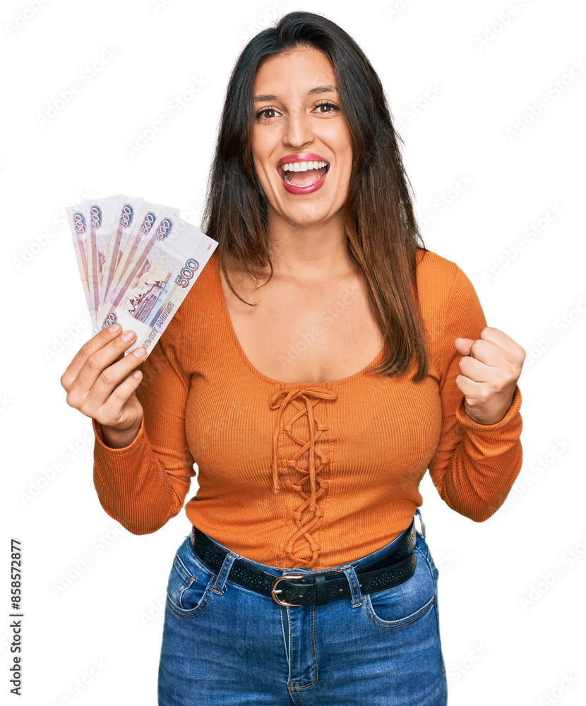 Beautiful hispanic woman holding russian 500 ruble banknotes screaming proud, celebrating victory and success very excited with raised arms Beautiful hispanic woman holding russian 500 ruble banknotes screaming proud, celebrating victory and success very excited with raised arms