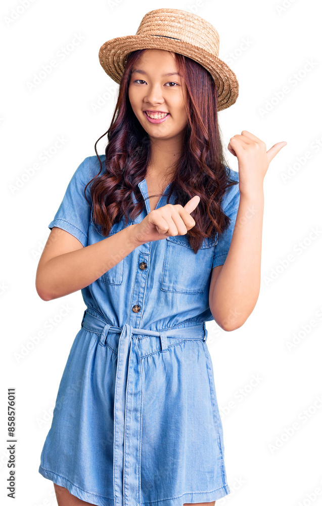 Young beautiful chinese girl wearing summer hat pointing to the back behind with hand and thumbs up, smiling confident Young beautiful chinese girl wearing summer hat pointing to the back behind with hand and thumbs up, smiling confident