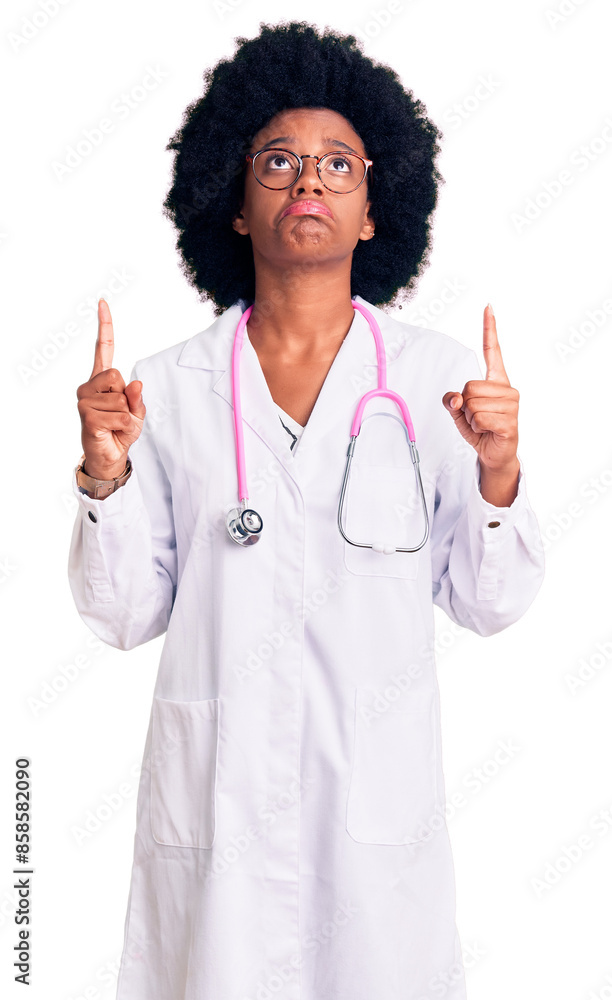 Φωτογραφία Young african american woman wearing doctor coat and stethoscope pointing up looking sad and upset, indicating direction with fingers, unhappy and depressed