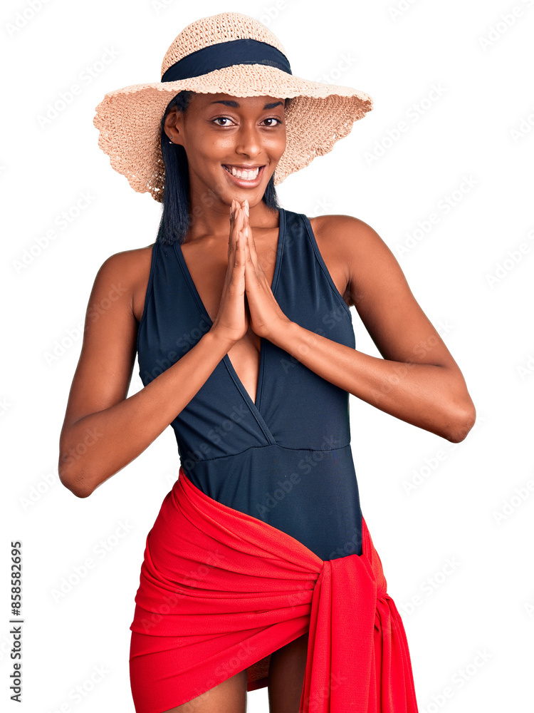 Young african american woman wearing swimsuit and summer hat praying with hands together asking for forgiveness smiling confident. Young african american woman wearing swimsuit and summer hat praying with hands together asking for forgiveness smiling confident.