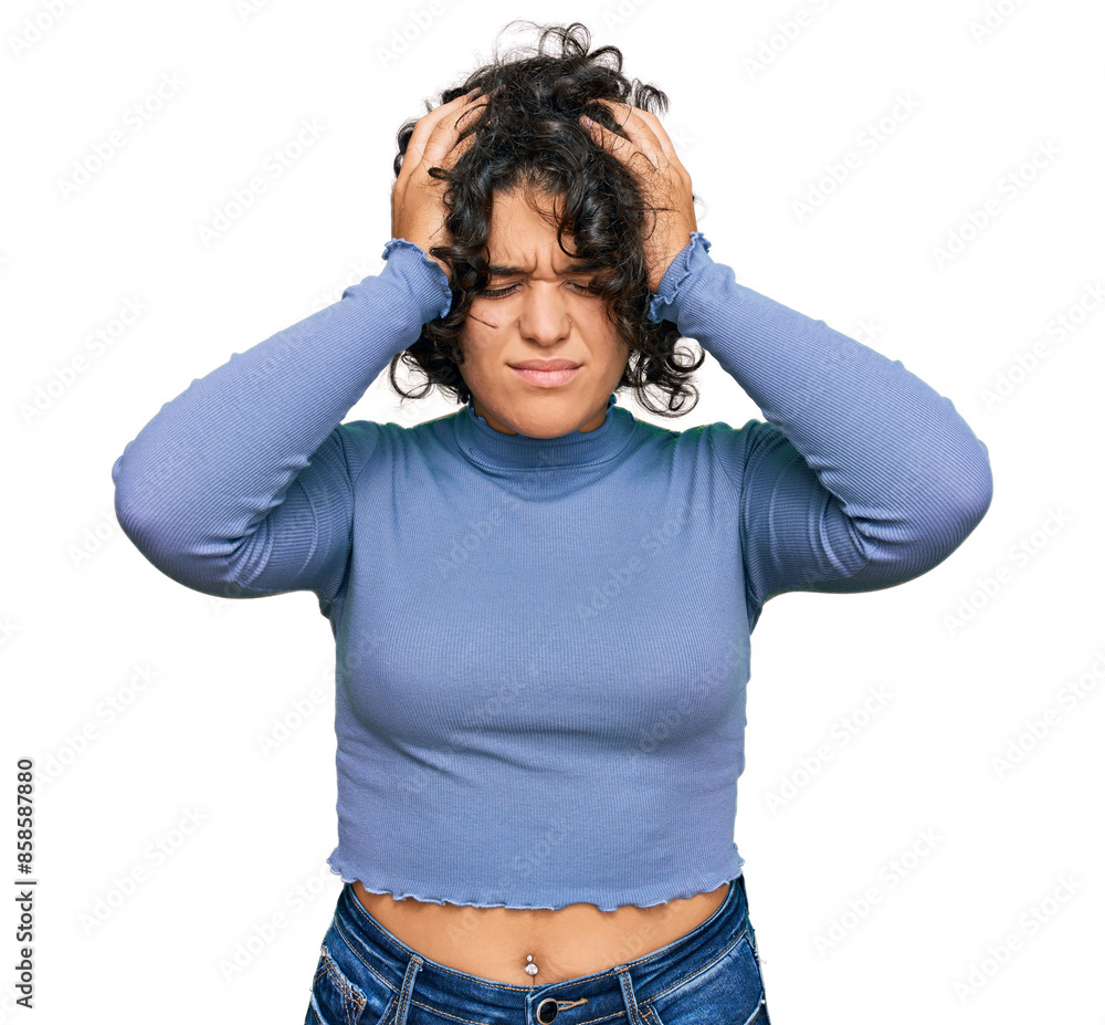 Young hispanic woman with curly hair wearing casual clothes suffering from headache desperate and stressed because pain and migraine. hands on head. Young hispanic woman with curly hair wearing casual clothes suffering from headache desperate and stressed because pain and migraine. hands on head.