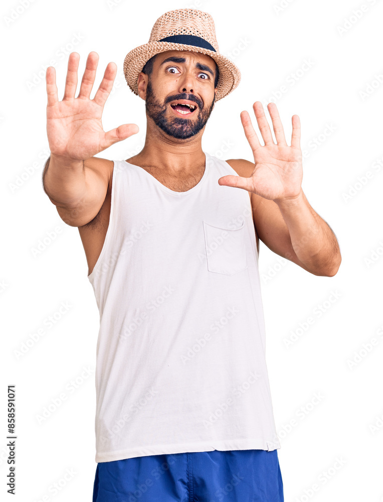 Young hispanic man wearing casual summer hat afraid and terrified with fear expression stop gesture with hands, shouting in shock. panic concept. Young hispanic man wearing casual summer hat afraid and terrified with fear expression stop gesture with hands, shouting in shock. panic concept.