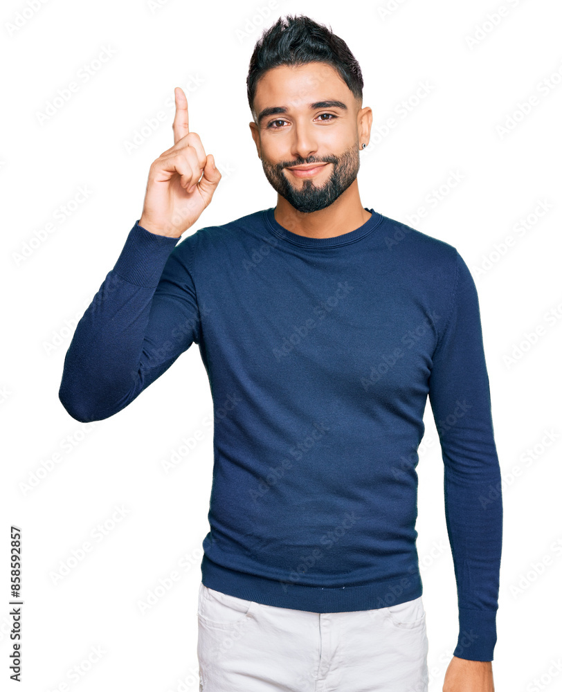 Naklejka premium Young man with beard wearing casual blue winter sweater pointing finger up with successful idea. exited and happy. number one.