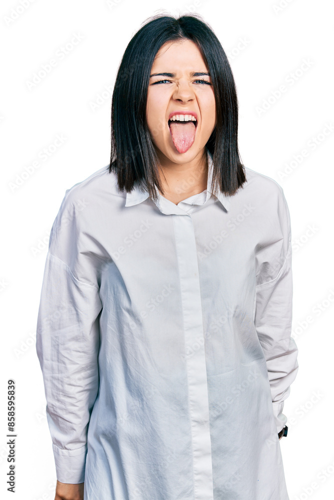 Young brunette woman with blue eyes wearing oversize white shirt sticking tongue out happy with funny expression. emotion concept. Young brunette woman with blue eyes wearing oversize white shirt sticking tongue out happy with funny expression. emotion concept.