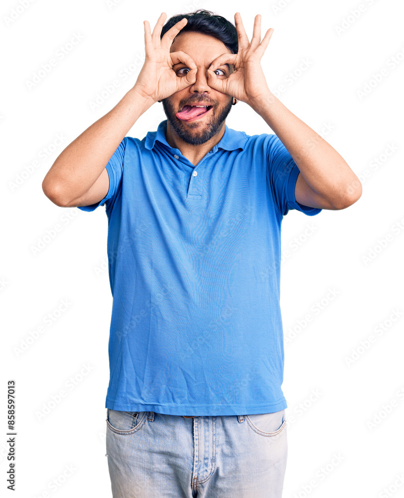 Young hispanic man wearing casual clothes doing ok gesture like binoculars sticking tongue out, eyes looking through fingers. crazy expression. Young hispanic man wearing casual clothes doing ok gesture like binoculars sticking tongue out, eyes looking through fingers. crazy expression.