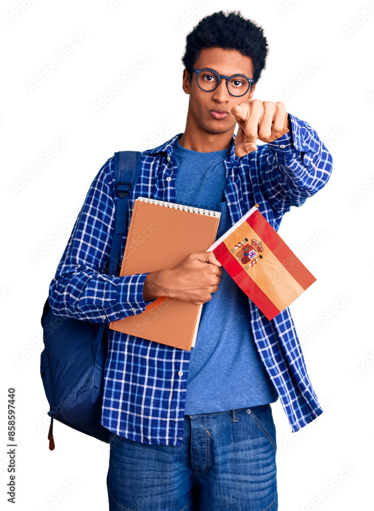 Young african american man wearing student backpack holding spanish flag pointing with finger to the camera and to you, confident gesture looking serious Young african american man wearing student backpack holding spanish flag pointing with finger to the camera and to you, confident gesture looking serious
