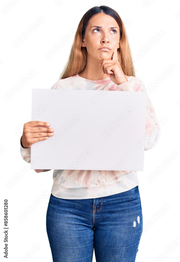 Beautiful young woman holding blank empty banner serious face thinking about question with hand on chin, thoughtful about confusing idea Beautiful young woman holding blank empty banner serious face thinking about question with hand on chin, thoughtful about confusing idea