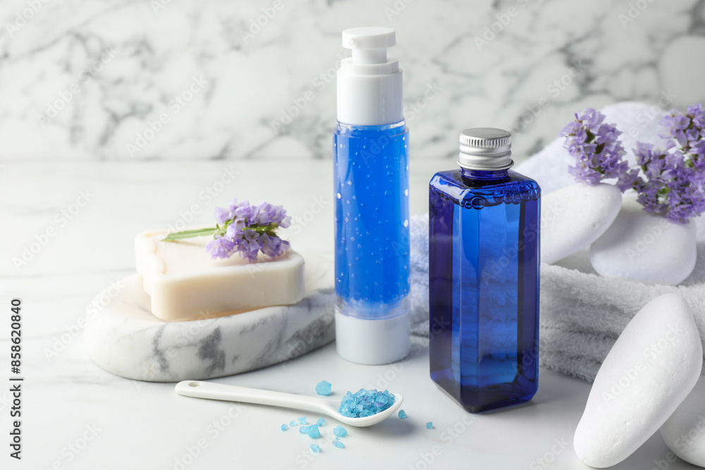 Spa composition. Bottles of cosmetic products, sea salt, stones, soap and flowers on white marble table Spa composition. Bottles of cosmetic products, sea salt, stones, soap and flowers on white marble table