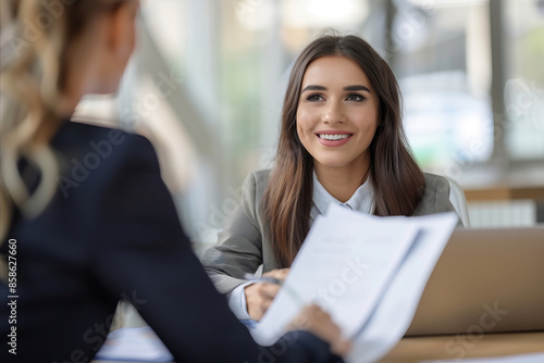 Free Download A business woman sitting at a table in an office holding documents while being interviewed - GFXLoad