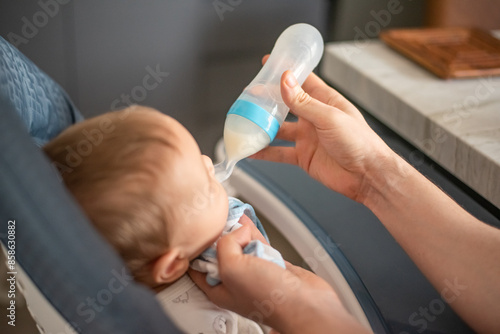 Father feeds baby with silicone feeding bottle with spoon when mother returns to work