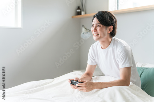 家のベッドルーム・寝室でゲームをする男性ゲーマー（不摂生・遊ぶ・ストレス解消）
 photo