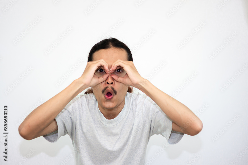 Young man wearing casual gray t-shirt doing ok gesture like binoculars. eyes looking through fingers. Young man wearing casual gray t-shirt doing ok gesture like binoculars. eyes looking through fingers.