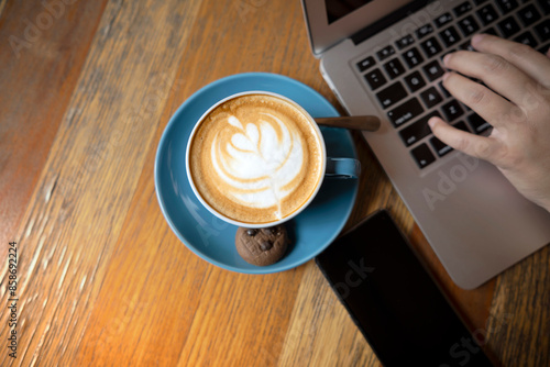A laptop is open on a wooden table with a blue coffee cup