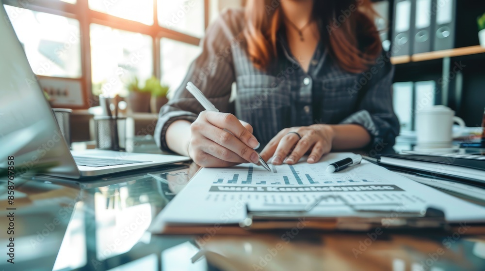 Hands writing notes on a notepad at an office desk with a laptop and other work documents in the background Hands writing notes on a notepad at an office desk with a laptop and other work documents in the background