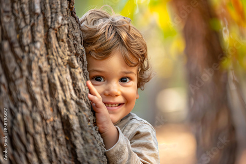 a little boy is peeking out from behind a tree © Nam