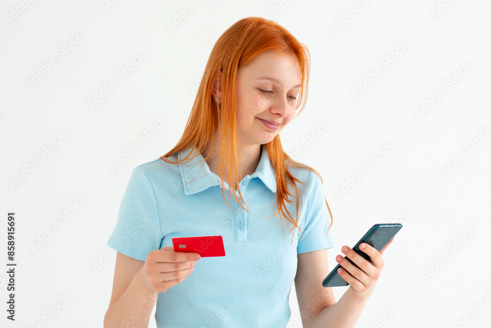 Cheerful young girl showing plastic credit card while using mobile phone isolated over white background, wearing blue t-shirt Cheerful young girl showing plastic credit card while using mobile phone isolated over white background, wearing blue t-shirt
