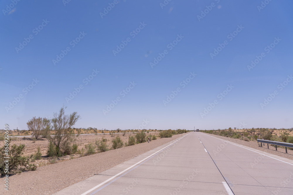 A road with a clear blue sky above it. The road is empty and there are no cars on it